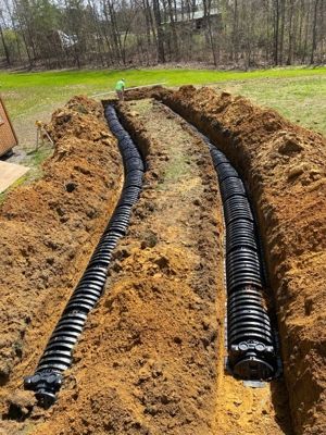 Two long excavated trenches with black chamber drain field lines installed across a grassy lot